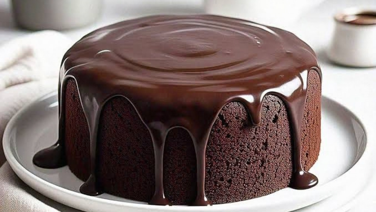 Bolo de chocolate redondo com cobertura brilhante de ganache escorrendo pelas laterais, sobre um prato branco
