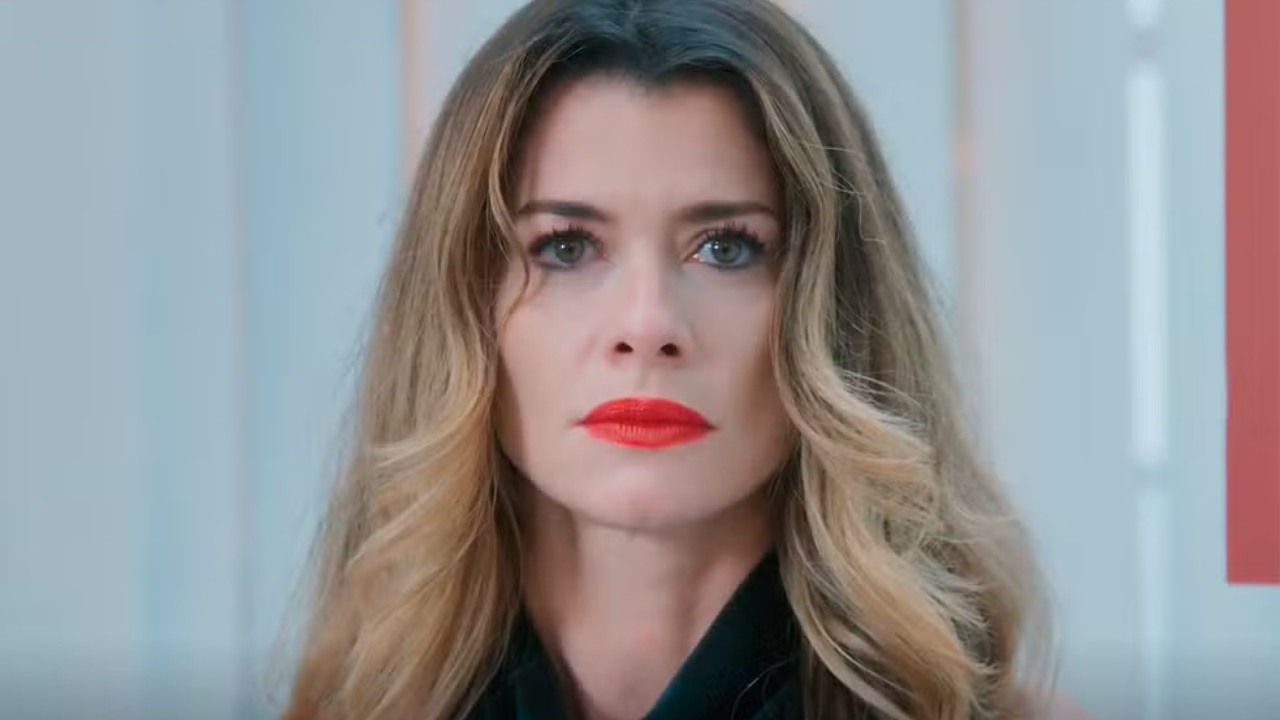 Mulher de cabelos loiros ondulados e maquiagem forte, com batom vermelho vibrante, olhando diretamente para frente com expressão séria