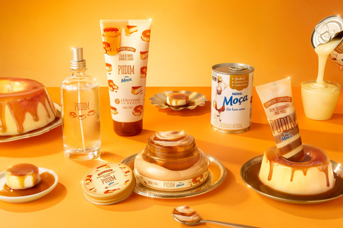 Produtos de beleza LOccitane au Brésil com fragrância de pudim, incluindo sabonete líquido, perfume, hidratante corporal e creme para mãos, dispostos com pudins de verdade e latas de Leite Moça sobre um fundo laranja
